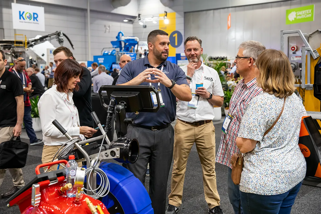 No Dig Conference Visitors talking with an exhibitor beside a red and blue pipe inspection reel at No Dig NZ Conference