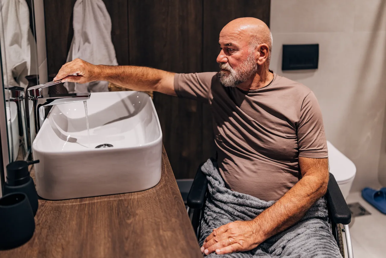 senior-man-wheelchair-reaching Senior man in a wheelchair reaching for the tap at a bathroom basin